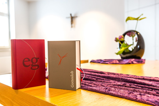 Seelsorge am Bergmannsheil Buer: In der Kapelle stehen auf einem Tisch zwei Bücher und ein Blumenarrangement. Im Hintergrund an der Wand hängt das christliche Kreuz.