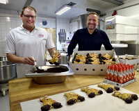 Zwei Bäcker stehen in der Backstube vor vielen Hefe-Osterhasen und bestreichen das Gebäck mit Schokolade.